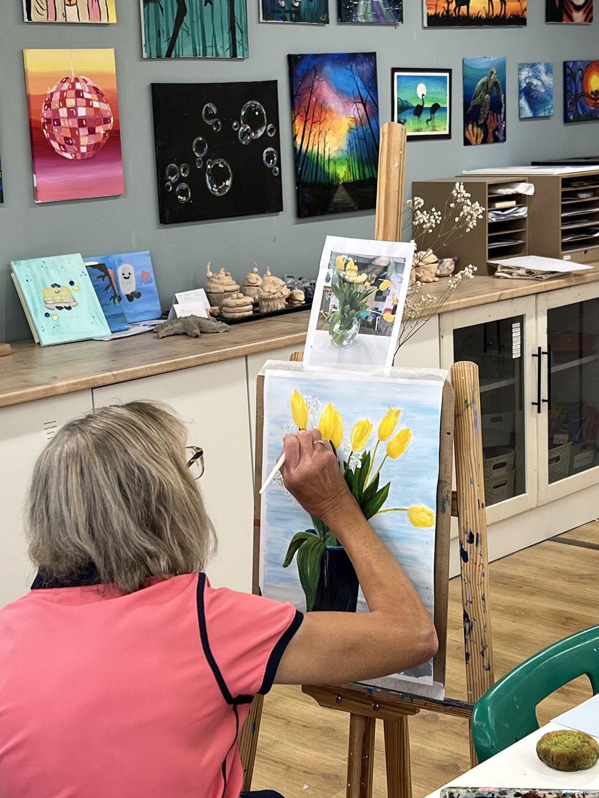Adult student painting yellow tulips in a vase at an easel in the studio