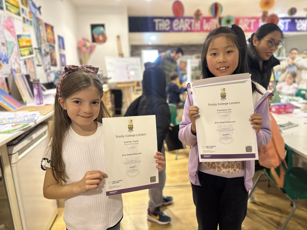 Two smiling students holding their Arts Award certificates in The Art School studio