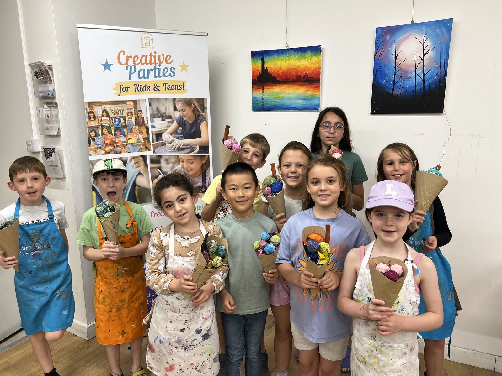 A group of smiling children in aprons at a Creative Party, holding the flower bouquets they made