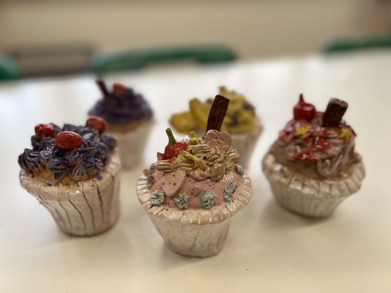 Glazed clay cupcakes with colourful icing and cherries, made by children